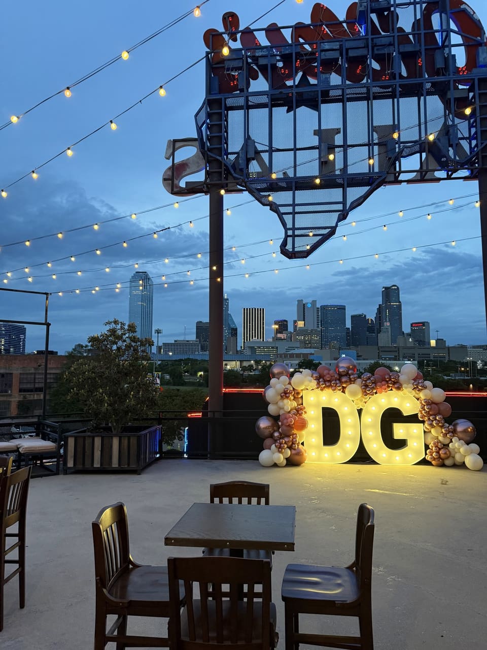 Lighted marquee letters with florals on a rooftop with the Dallas skyline