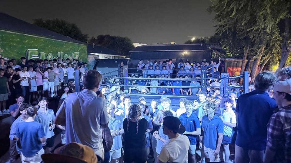 Packed crowd around a lit boxing ring at an outdoor fight night