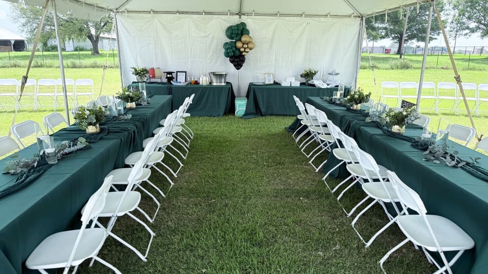 Long tented dining tables with white chairs set for a countryside celebration