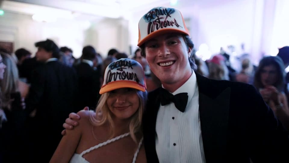 Couple in a tuxedo and gown wearing matching party hats at a black tie gala