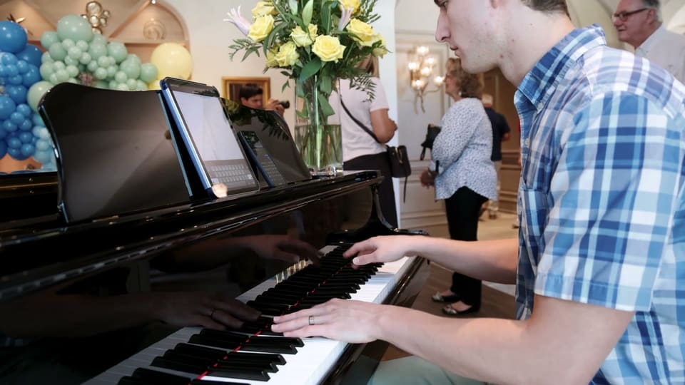 Guest playing a grand piano beside a balloon garland at an at-home birthday party